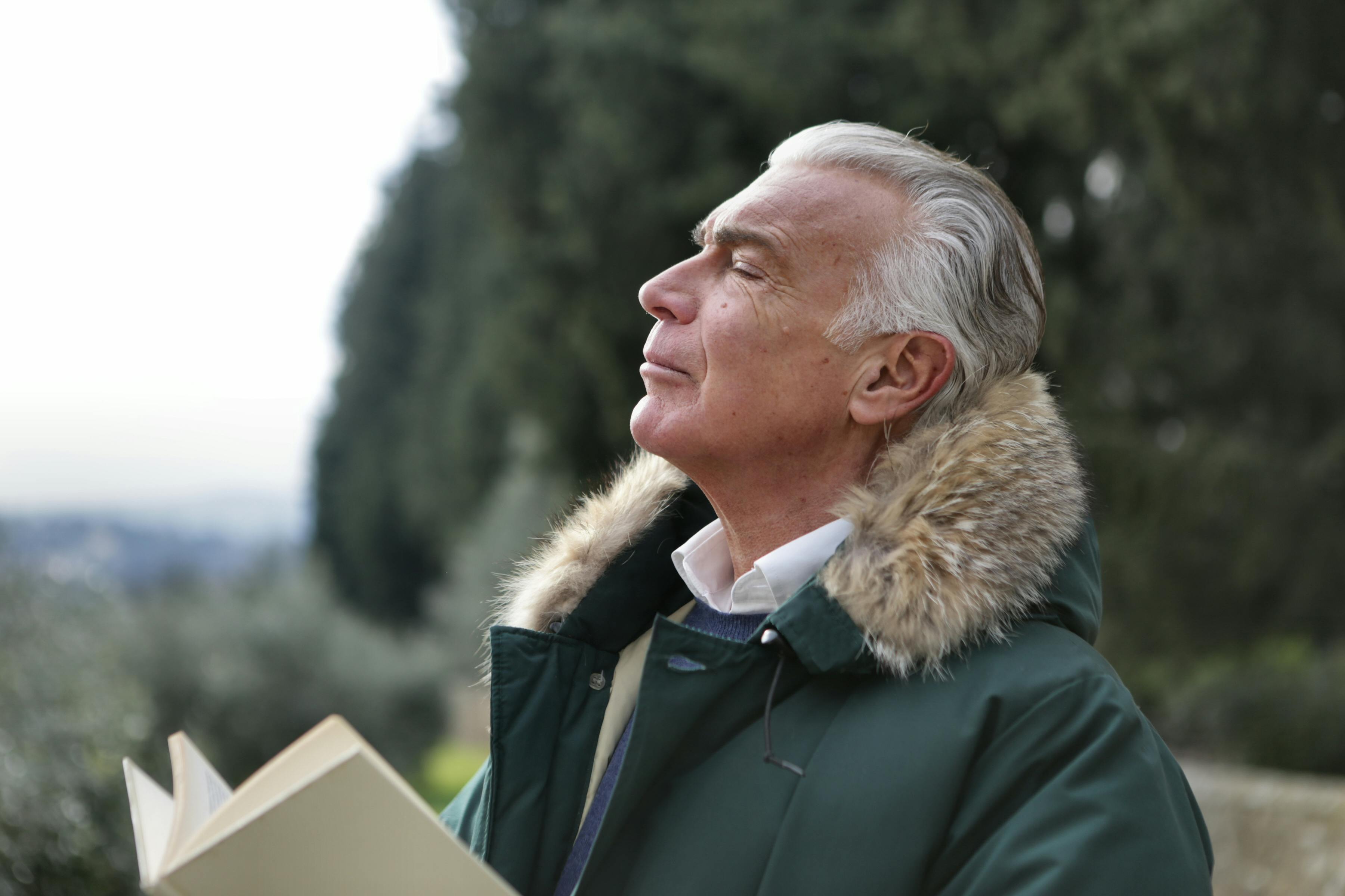 An older man reading a book and inhaling deeply with his eyes closed